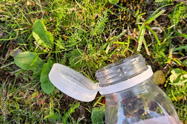 Obraz A discarded bottle with a tethered cap on the grass. EU regulation initiative on attached plastic bottle caps for better recycling and reducing pollution, environmental litter