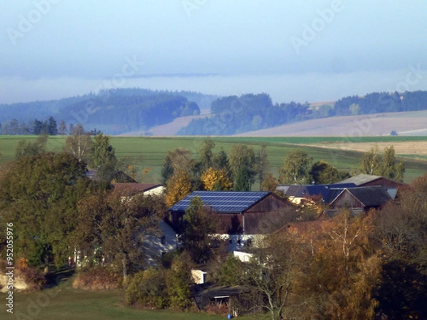 Obraz View of rural houses with solar panels on the roofs. Small hills and fields can be seen in the distance. Green energy and environmental protection