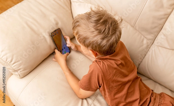 Fototapeta Close up of teenage boy playing mobile game online via smartphone sitting on sofa