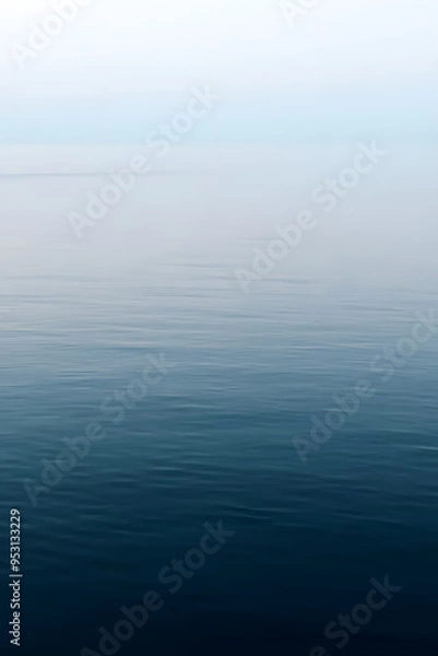 Fototapeta A serene view of calm water with gentle ripples, reflecting a soft blue hue. The surface appears smooth and tranquil, creating a peaceful atmosphere.