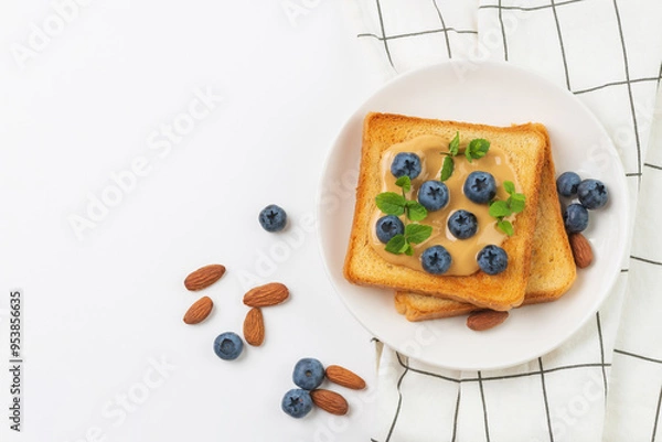 Fototapeta Toast with peanut butter, blueberries and fresh mint on white plate with napkin. Sandwich  for breakfast top view with copy space.