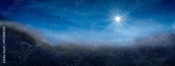 Fototapeta Bright star indicates the Nativity of Jesus Christ in the starry sky and fog rises in the mountains above the night forest.