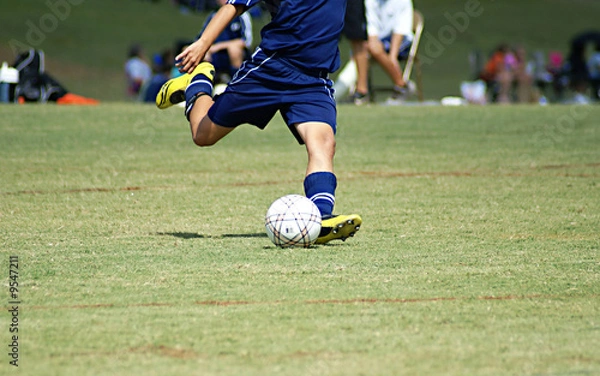 Fototapeta Young boy strking a soccer ball in a game.