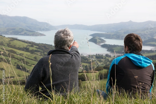 Fototapeta Two men sit on the top of hill and look at harbour, view from be