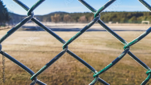 Fototapeta Frozen fence with frost next to a field on a very cold winter morning