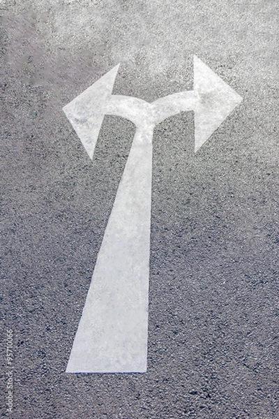 Fototapeta A two way arrow symbol on a black asphalt road surface.