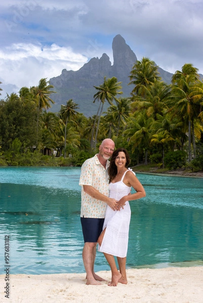 Obraz Happy, middle aged couple together on vacation on tropical island Bora Bora. Palm trees, an azure ocean lagoon and Mount Otemanu can be seen in the background. 