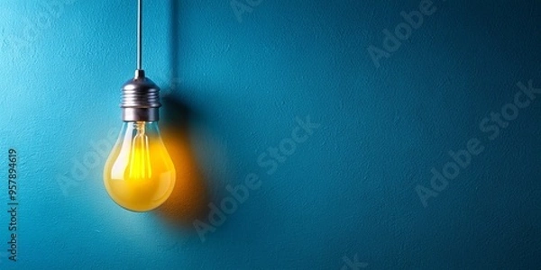 Fototapeta A yellow light bulb hanging from a blue wall creating a minimalist and artistic look