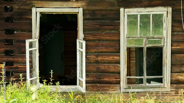 Fototapeta broken windows of an abandoned village house overgrown with grass