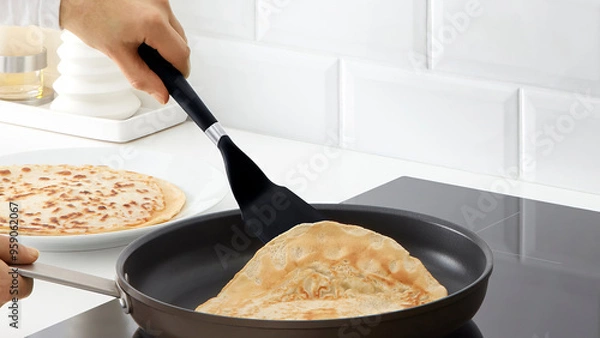 Fototapeta Closeup of a person flipping pancakes in a frying pan.