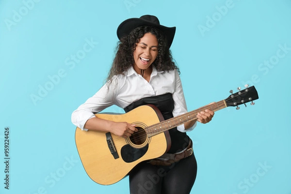Fototapeta African-American cowgirl playing guitar on blue background