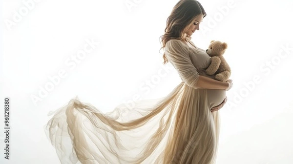 Fototapeta Pregnant woman in a flowing dress, standing with a teddy bear cradled in her arms, looking down lovingly, isolated on a white background