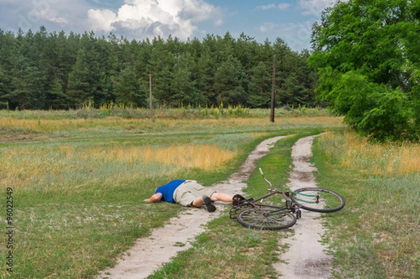 Fototapeta man lying on a country road after he fallen down from an ancient bicycle