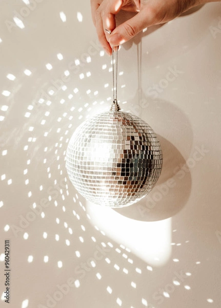 Fototapeta Close-up of a hand holding a disco ball, casting reflections and light patterns on the background