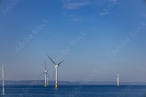 Fototapeta Abstract ethereal view of beautiful giant wind turbines at sea with patchy fog blue sky