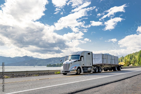 Obraz Bonnet powerful white big rig semi truck transporting covered fastened cargo on flat bed semi trailer running on the road along the railroad and river