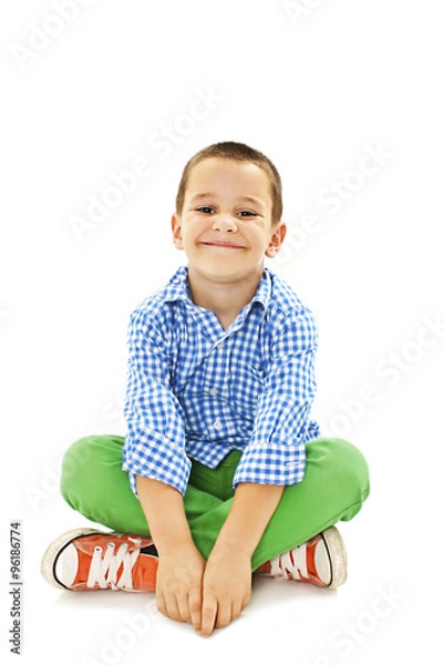 Obraz Smiling little boy sitting down on floor and looking at camera. Isolated on white background 