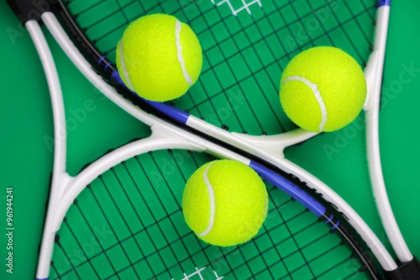 Fototapeta Two lawn tennis rackets are lying next to each other on a green background, yellow tennis balls are lying on them, close-up. The concept of sports and games. High quality photo