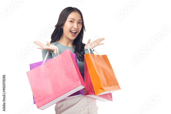 Fototapeta Cheerful young woman holding colorful shopping bags in both hands, expressing joy and excitement. Set against a clean white background, her enthusiasm captures the fun of a successful shopping spree