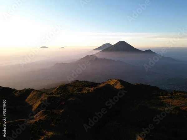 Fototapeta Aerial views of Mount Sindoro and Mount Sumbing in the distance from peak of Mount Prau, Dieng, Wonosobo, Indonesia with soft mist on the mountain slopes and red sky at dawn.