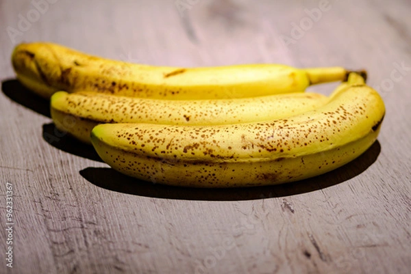 Fototapeta Photo of a set of 3 ripe bananas with brown spots on a gray table.