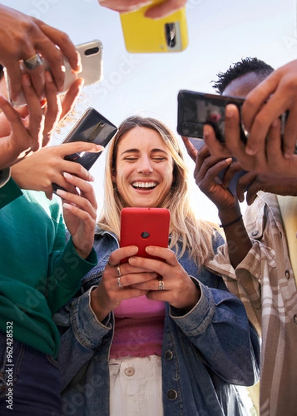 Fototapeta Low angle view of a group of young teenagers friends using cell phones and walking in the city. Concept of community millennial people addicted to technology. Social Media communication generation Z