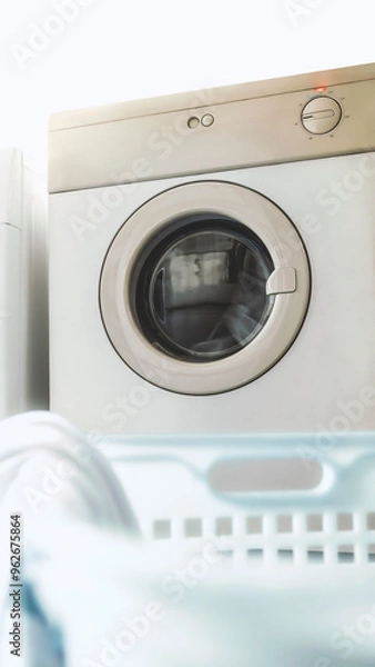 Fototapeta Electric clothes dryer machine in laundry room. Routine chores. Pile of clothes in basket. Housework concept