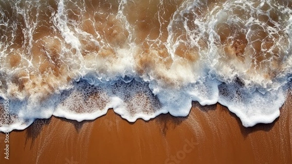 Fototapeta Aerial view of ocean waves crashing onto a sandy beach, creating white foam patterns