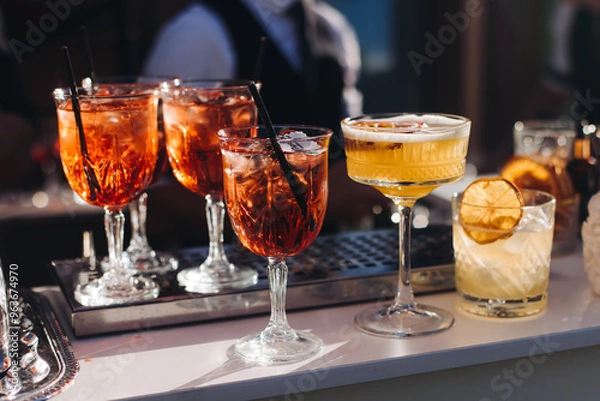 Fototapeta Bartender working, beautiful row line of different coloured liquor alcohol cocktails on a open air party in a bar, and others on catering banquet on event, barman mixing drinks and beverages in club