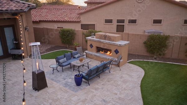 Fototapeta An aerial view of a desert landscaped backyard featuring a travertine pool deck with an outdoor kitchen, fireplace, pool and spa.