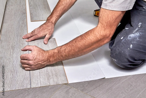 Fototapeta Man laying laminate flooring.Installing laminate floor, detail on many hands holding wooden tile, over white foam base layer.