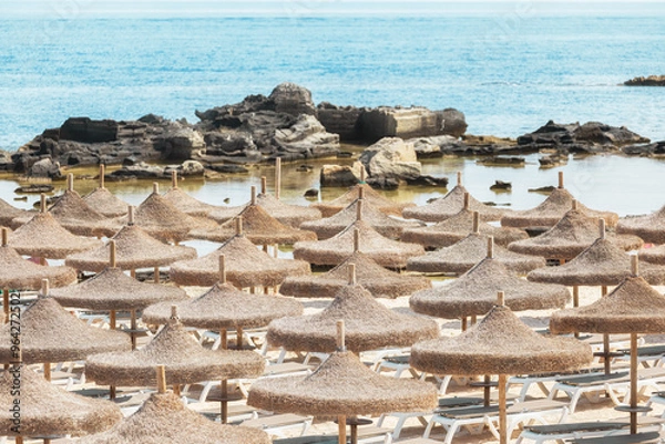 Fototapeta Straw umbrellas on the beach and turquoise water on a sunny day.