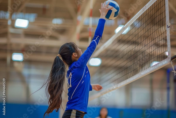 Obraz Girl in a blue shirt is about to hit a volleyball. The girl is wearing a ponytail and is reaching for the ball