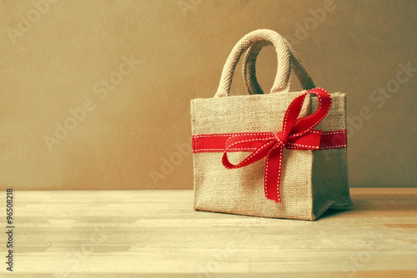 Obraz Beautiful gift bag with red bow on wood background and color filters