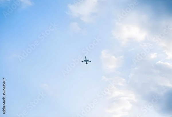 Fototapeta Airplane flying high in a clear blue sky with fluffy white clouds.