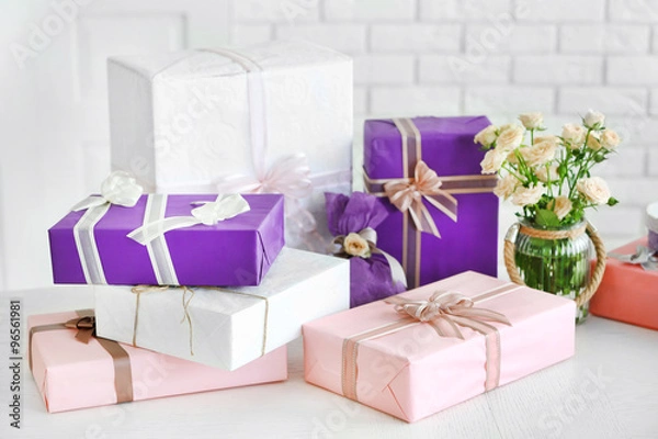 Fototapeta Composition of colourful gift boxes and flowers in glass on white table in front of brick wall background