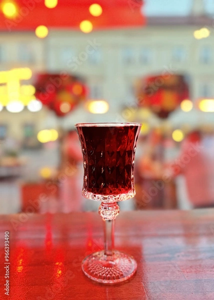 Obraz Beautiful carved crystal glass with cherry wine is on the table in a blurred bright background.