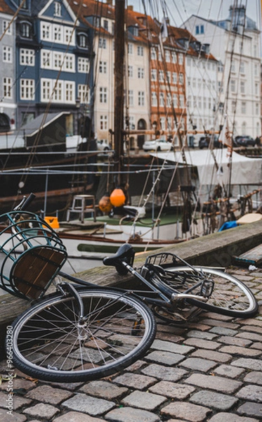 Fototapeta A bike dropped on the ground next to Nyhavn, Copenhagen. The waterfront, buildings and boats of the harbour are in the background.