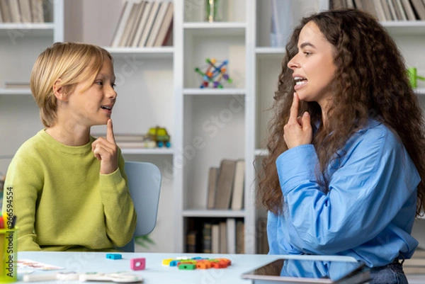 Fototapeta Blonde boy exercising with speech therapist and making efforts