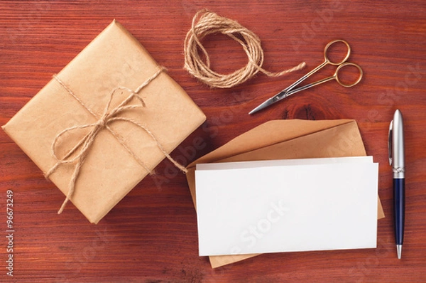 Obraz Gift box and envelope with blank paper sheet decorated accessories on wooden table