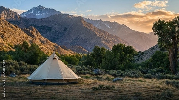 Obraz A tourist camp in the mountains showcases a spacious tent surrounded by lush vegetation and rugged peaks during a tranquil evening amidst nature’s beauty