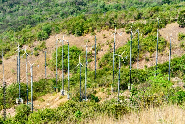 Fototapeta Wind power on the mountain and blue sea on a clear sky background morning day at Koh Larn island. View point on mountain to see view of windmill and sky. Wind turbine. Wind Energy. Pattaya, Thailand.