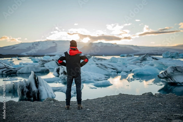 Obraz A man in a winter jacket and hat, standing against a backdrop of glaciers and a lake.