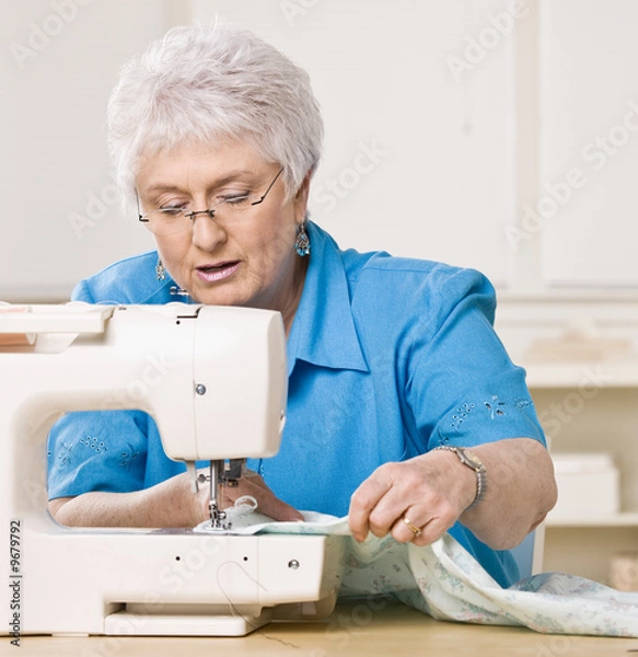 Obraz Senior woman using sewing machine at home