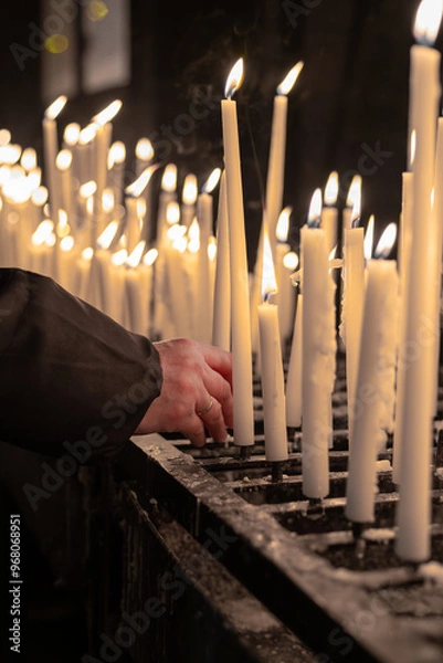 Obraz Arm and hand of a person placing a burning candle at an altar in a church.