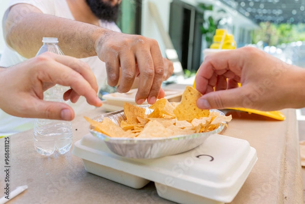 Fototapeta In a vibrant and lively scene, hands eagerly reach for delicious nachos, symbolizing the joy of shared moments and the lasting friendships that often develop over delightful and tasty food