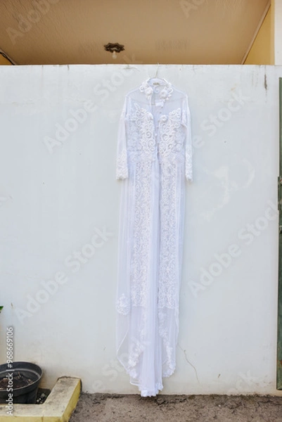 Fototapeta Wedding dress hanging on white wall