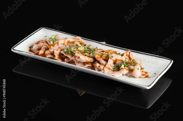 Fototapeta Deliciously plated gourmet dish of sliced grilled meat with garnish on a rectangular white plate, against a black background.