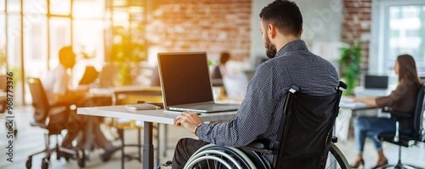 Fototapeta Man in wheelchair working on laptop in modern office.
