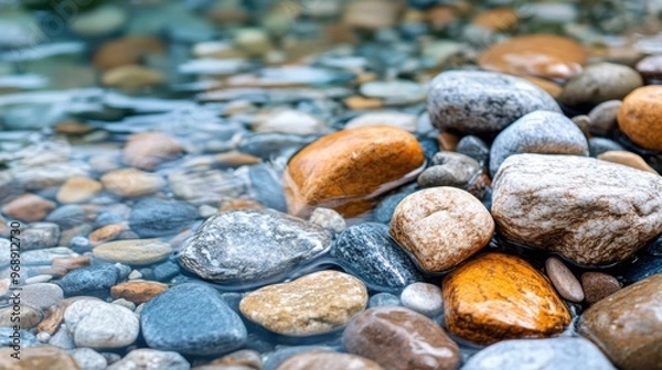 Fototapeta Close-up image of smooth, colorful pebbles in shallow water. The image shows the diversity of shades and textures of the wet stones with clear water flowing over them.